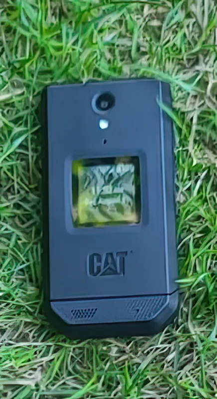 Closed in grass — the outer lid with the camera, cover display and CAT badge